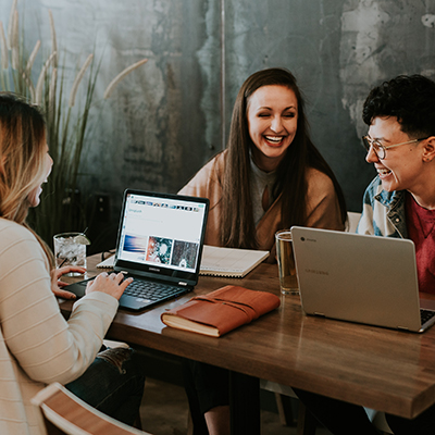 three smiling graduate students sit at a table with laptops