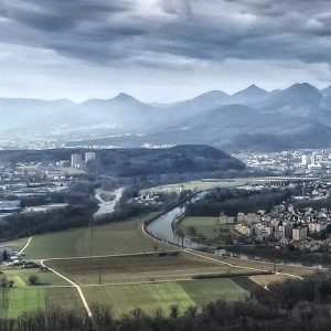 Many buildings in a valley with mountains in the background, and a river and roads across the landscape. Crop of a photo by Patrick Federi, via unsplash.