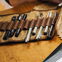 Pens in a leather roll-up pen holder laid out on a wood table. Detail of a photo by Rachael Gorjestani, via Unsplash.