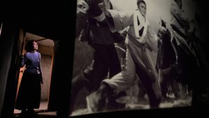 Still from Goodnight, Dragon Inn. Chen Shiang-chyi performs as the ticket taker, illuminated in the doorway of a darkened theatre in which a wuxia film, Dragon Inn, is projected in a large screen