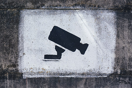 Stenciled image of a surveillance camera in black spray paint against a concrete wall