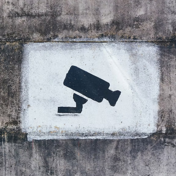 Stenciled image of a surveillance camera in black spray paint against a concrete wall