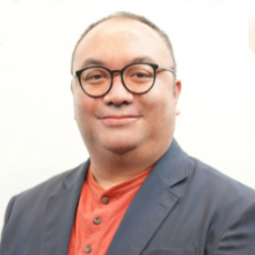 Dr. Andy Chi-on Chin wears an orange button-down shirt, grey blazer, and black-rimmed round glasses, smiling