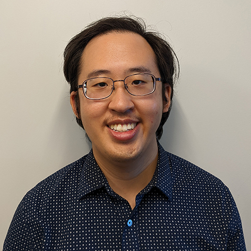 Stanley wearing a dark blue button-up collared shirt with dotted pattern, smiling