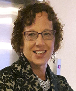 Esther Enkin wearing a collared jacket with black flowers and silver openwork choker-style necklace, smiling