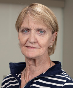 Kathy Gannon wearing a navy and white striped top and pearl stud earrings, smiling