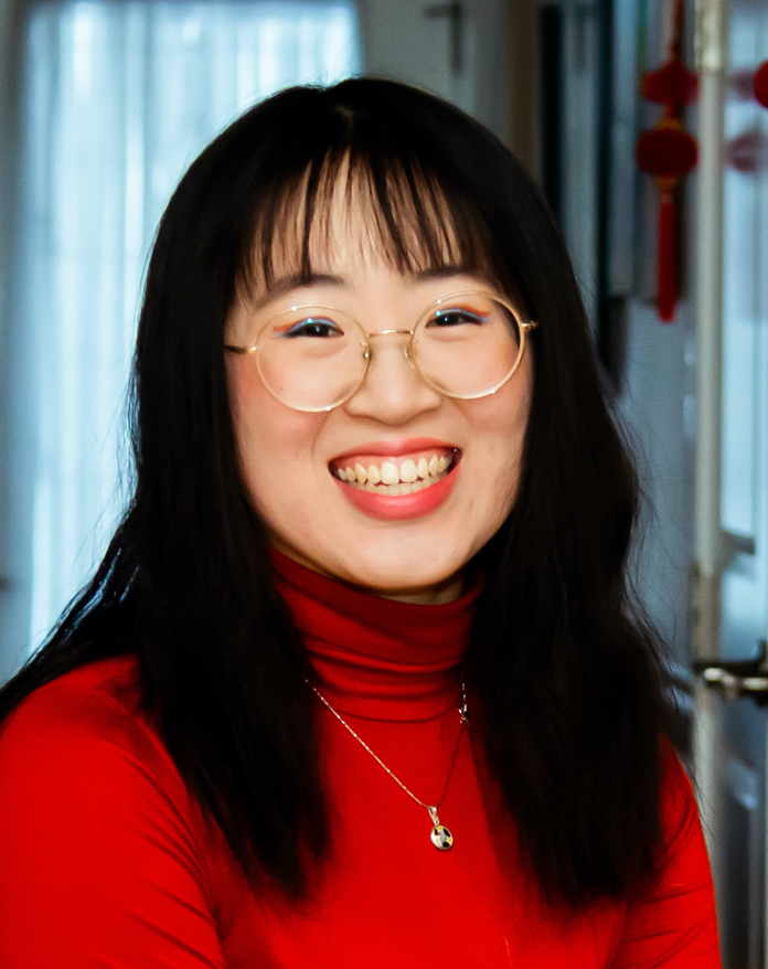 Photo of Ying wearing a bright red turtleneck shirt and smiling at the camera