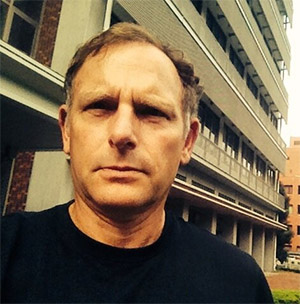Robert Markley in a dark crew-necked top outside a concrete building