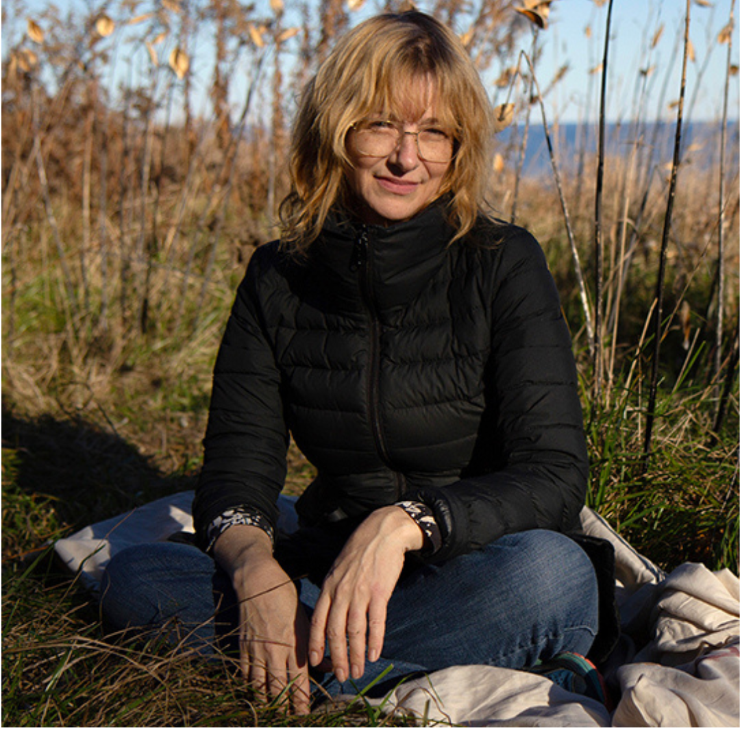 Prof. Althea Thauberger wearing a black top, blue jeans, and glasses, smiling